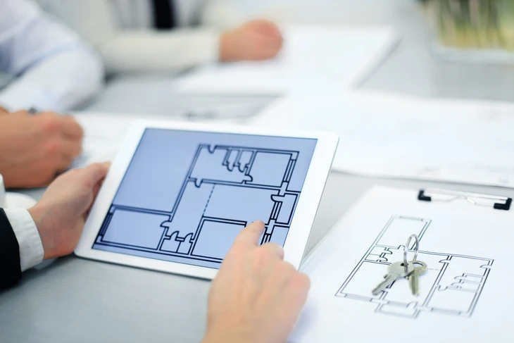 Professionnel en costume consultant des plans architecturaux sur tablette numérique et documents papier