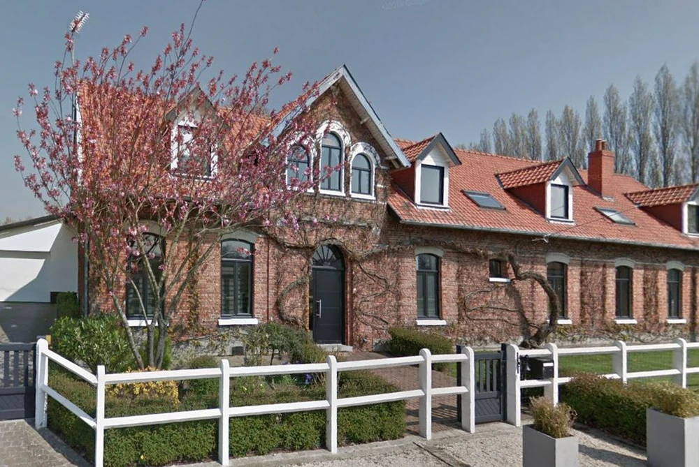 Maison individuelle en brique rouge avec toiture en tuiles, dotée de lucarnes et fenêtres à arcs cintrés