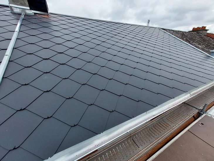 Toiture résidentielle moderne avec couverture en ardoises grises, lucarnes à volets noirs, cheminée maçonnée et fenêtres de toit