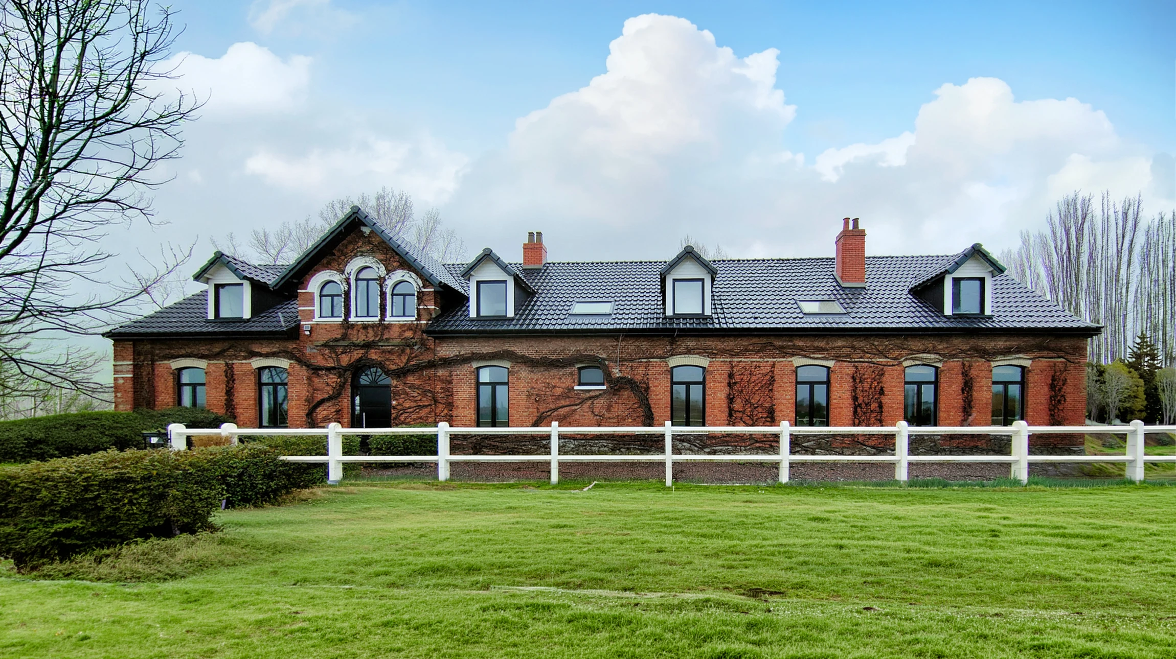 Sc&egrave;ne ext&eacute;rieure d'une maison traditionnelle en briques rouges avec toiture en tuiles ardoise, dormers et chemin&eacute;es