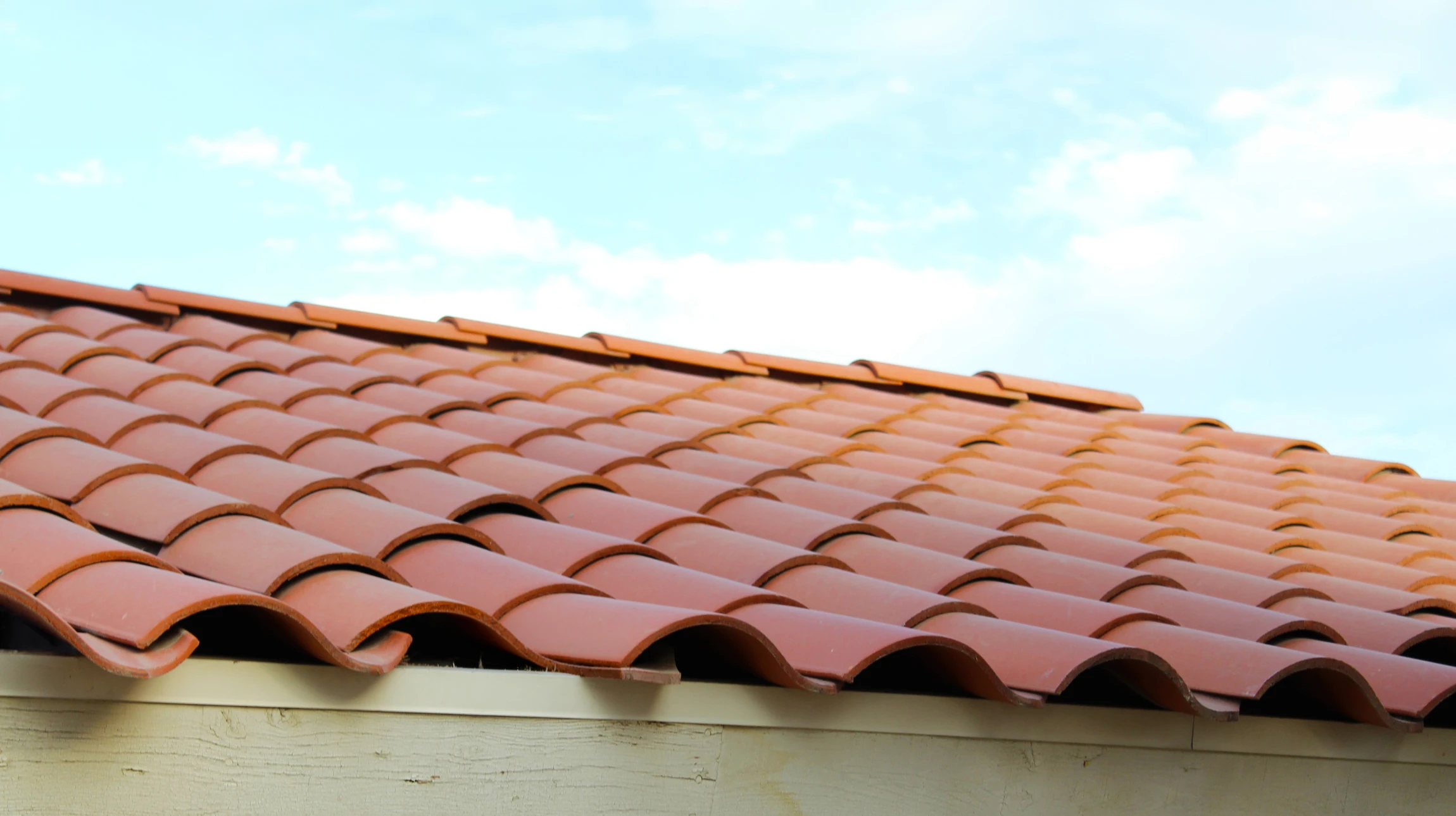 Deux couvreurs travaillent sur une toiture en pente, installant des tuiles terre cuite sur charpente bois apparente
