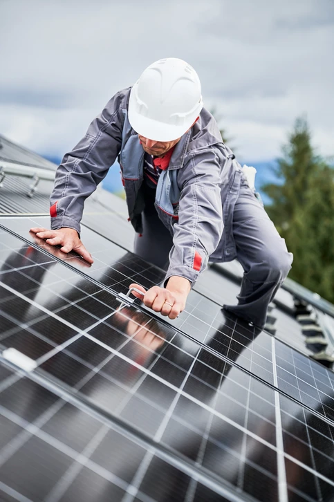 Deux techniciens en tenues de travail rouges installent des panneaux photovoltaïques sur une toiture en tuiles par temps ensoleillé