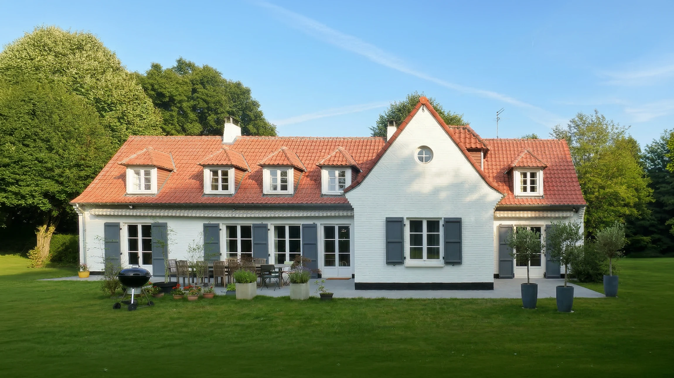Maison à colombages traditionnelle avec façade blanche et poutres en bois apparentes, toiture en tuiles rouges, volets marrons, balcon fleuri